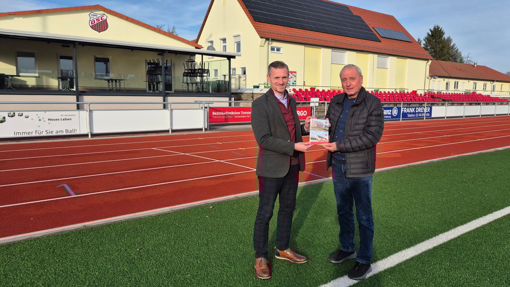 Dietrich Lehmann (rechts) übergibt Oscherslebens Bürgermeister Benjamin Kanngießer sein neues Buch über die Historie des Oscherslebener SC.