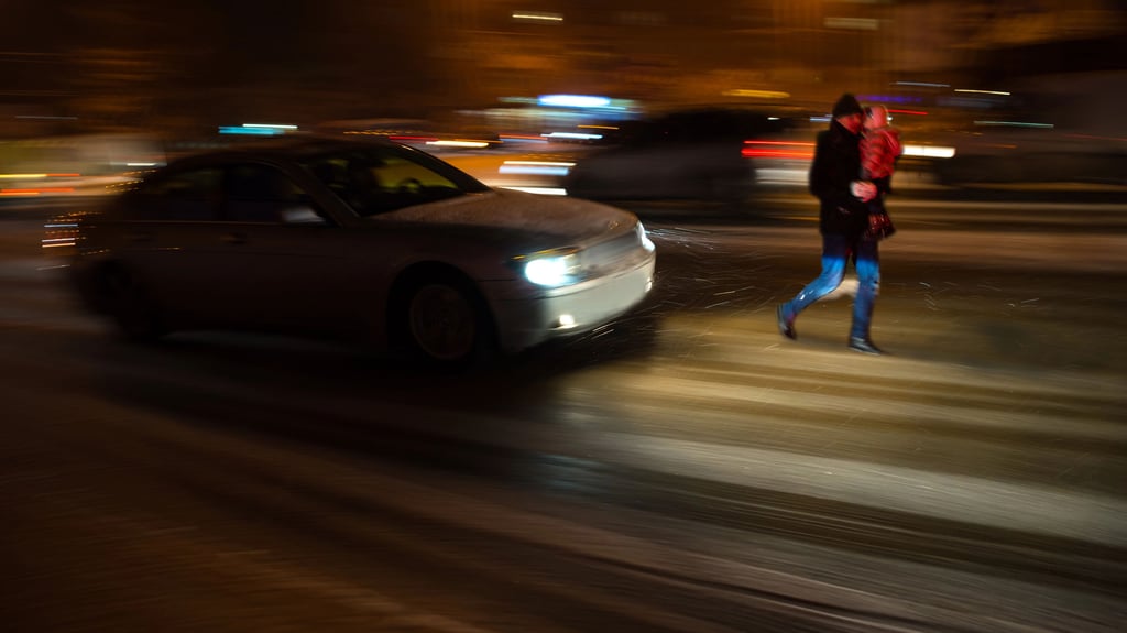 Ein Vater trägt sein Kind über den Zebrastreifen bei Dunkelheit: Gerade im Winter können schlechte Sicht und Missverständnisse im Straßenverkehr schnell zur Gefahr werden.