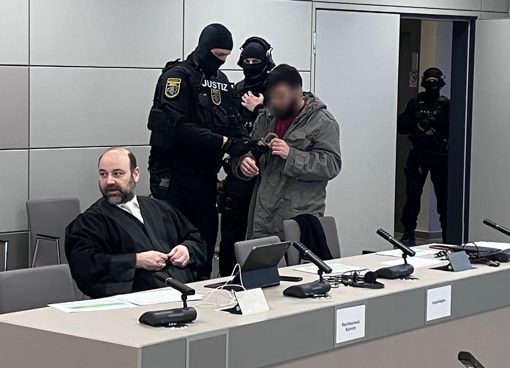 Azhar K. (4.v.li.) wird von Beamten einer Justiz-Spezialeinheit zu seinem Verteidiger in den Gerichtssaal geführt.