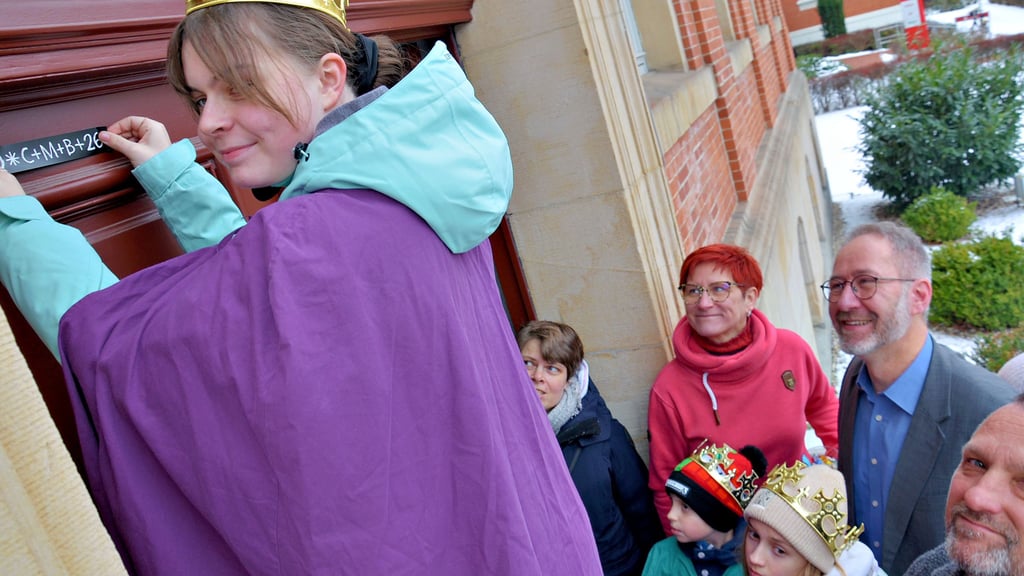 Annalena im Kostüm eines der drei Könige versieht das Staßfurter Rathausportal mit dem aktuellen Segensaufkleber.