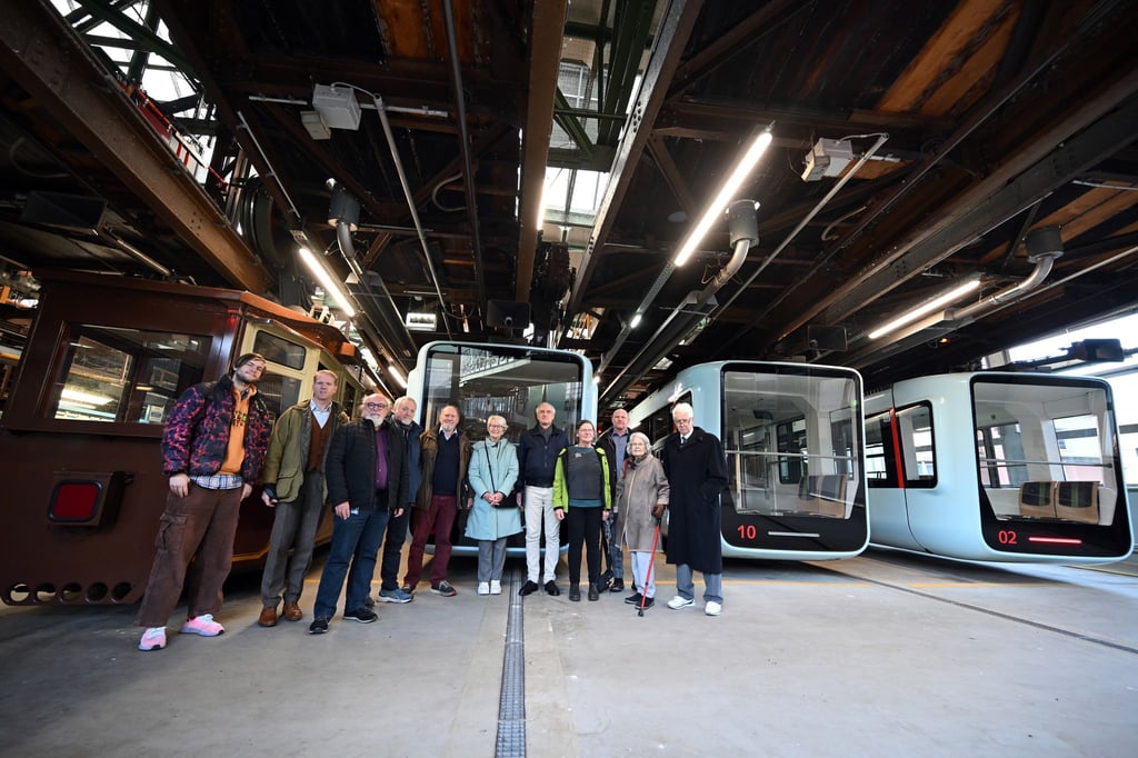 Vor Schwebebahn-Fahrzeugen der ältesten und jüngsten Generation stehen in Wuppertal Nachkommen und Verwandte des Schwebebahn-Erfinders Eugen Langen.