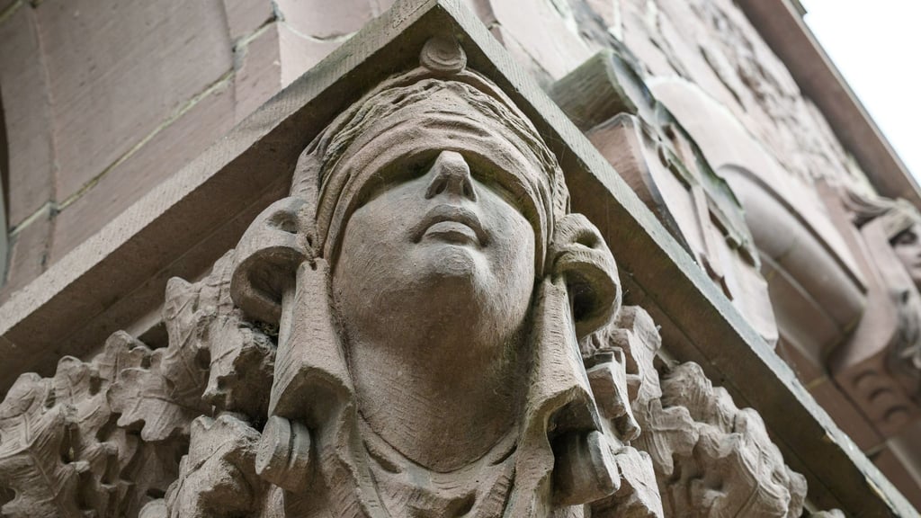 Ein Mann stirbt unerwartet im Amtsgericht Oldenburg. Eine Skulptur der Justitia hängt an einer Säule an dessen Eingang. (Symbolbild)