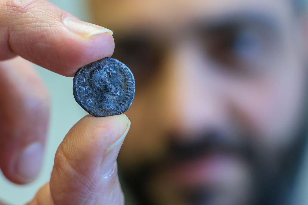 Ein Mitarbeiter des Landesamtes für Denkmalpflege und Archäologie präsentiert eine römische Münze aus dem frühen 3. Jahrhundert nach Christus.