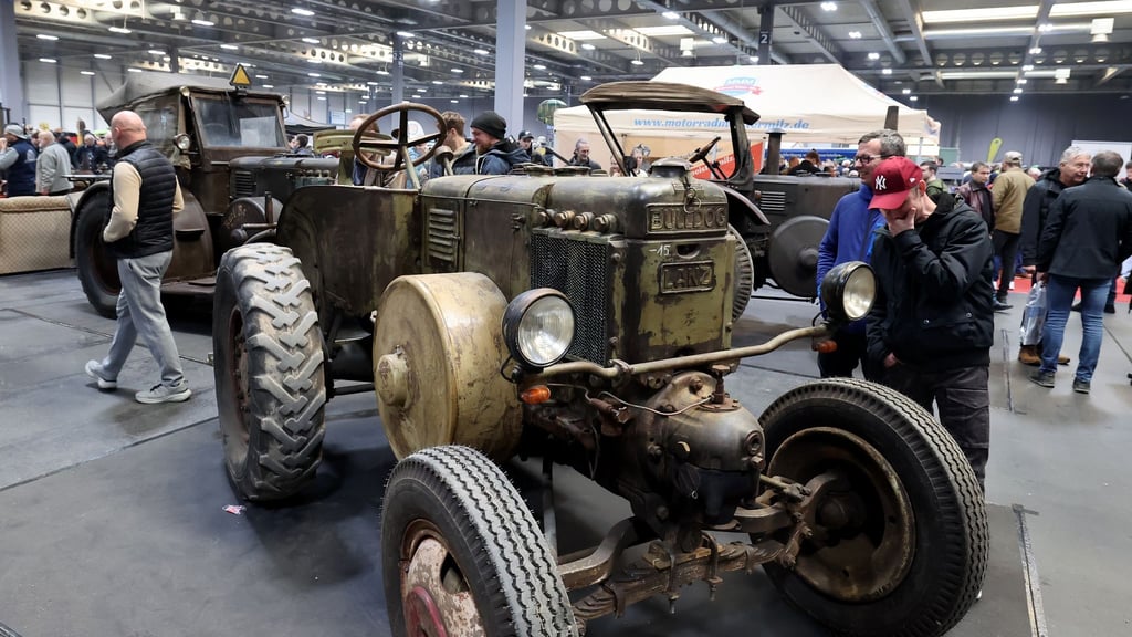 Hochglanzautos stehen auf der Messe neben alten Traktoren.