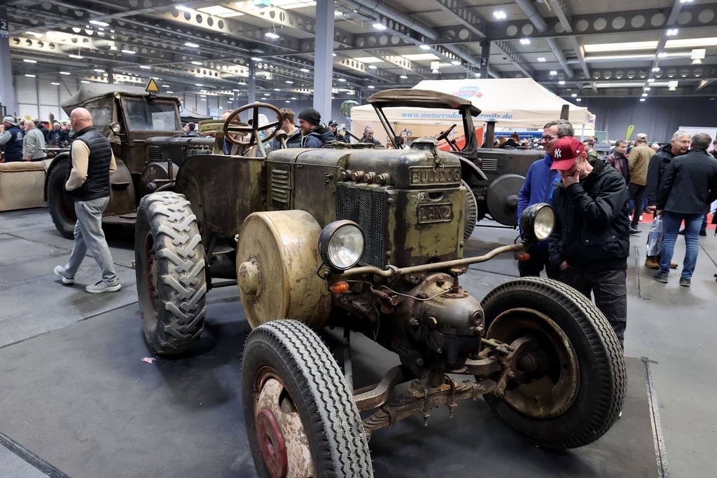 Hochglanzautos stehen auf der Messe neben alten Traktoren.