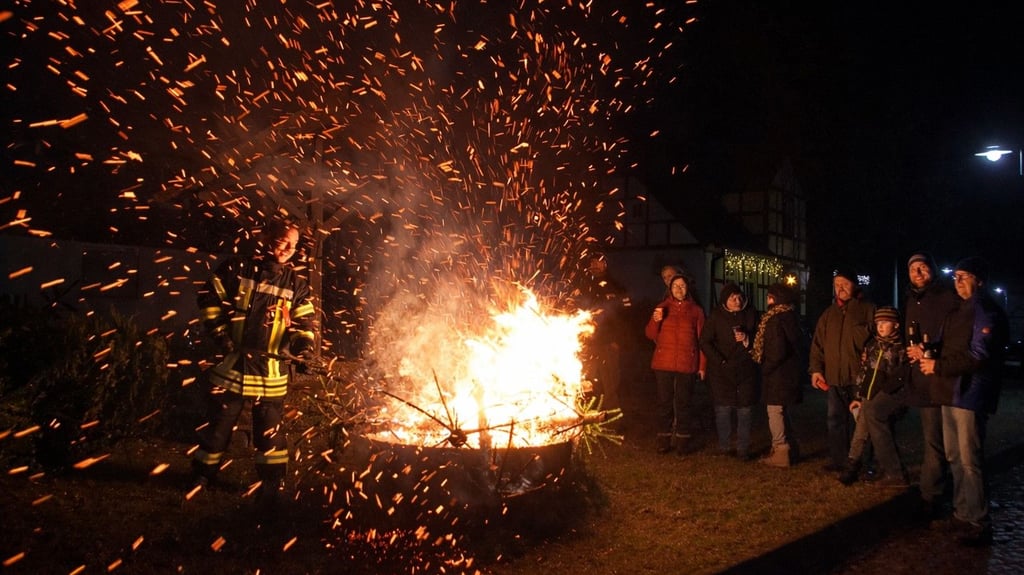Funkenflug und Feuerschein prägen das Weihnachtsbaumverbrennen in Grauingen. Zahlreiche Besucher wärmen sich am lodernden Feuer, während die Feuerwehrleute den sicheren Ablauf überwachen.