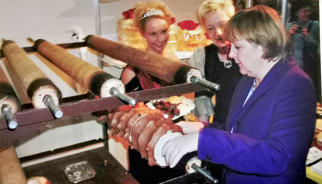Bettina Hennig (Mitte) zeigte Angela Merkel  auf der Grünen Woche 2005, wie der Kuchen von der Walze geschnitten wird.