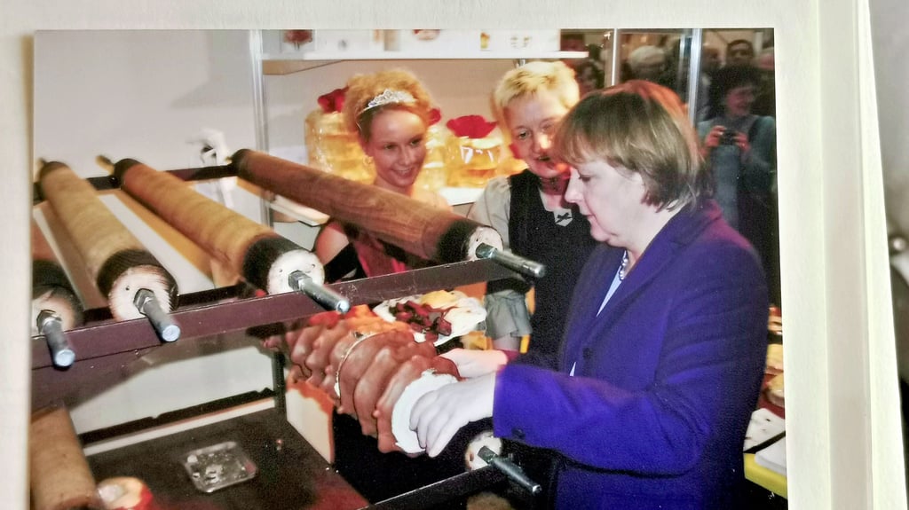 Bettina Hennig (Mitte) zeigte Angela Merkel  auf der Grünen Woche 2005, wie der Kuchen von der Walze geschnitten wird.