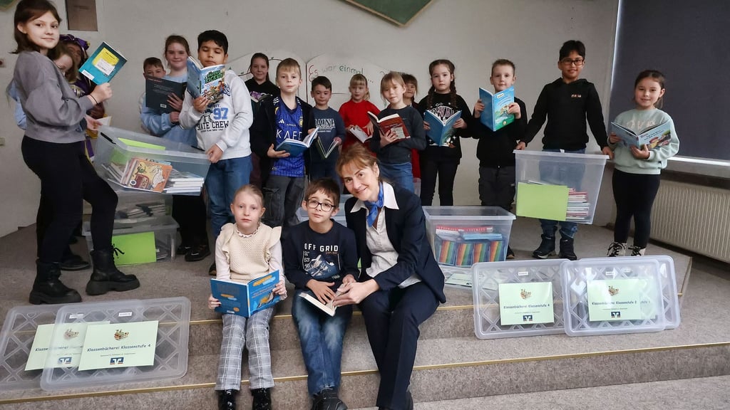 Leni und Luca schauen mit Volksbank-Vorständin Carmen Claus in die neuen Bücher, die jede Klasse der Grundschule Südwest in Sangerhausen bekommen hat.