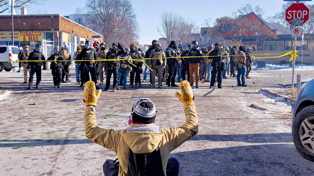 Ein Demonstrant sitzt mit erhobenen Armen auf der Straße vor Bundesbeamten in Minneapolis (USA). 