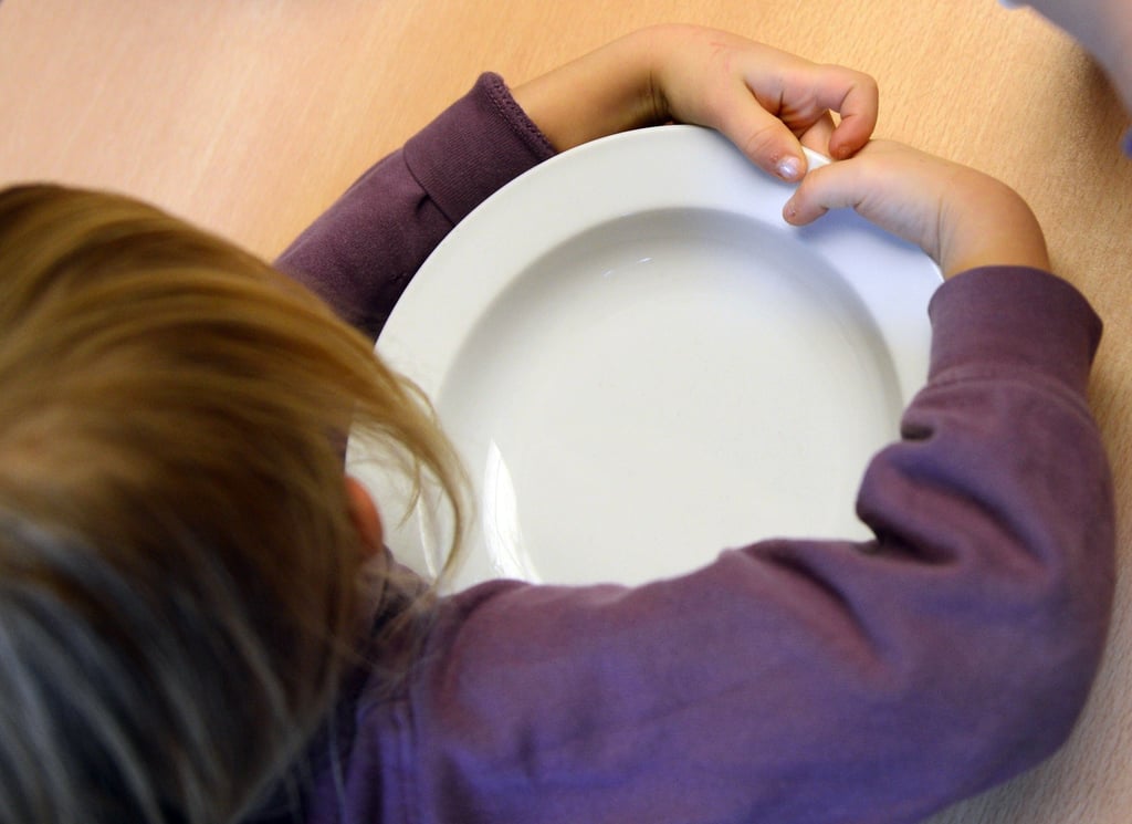 Ein Kind umklammert seinen leeren Teller und wartet auf das Mittagessen. Immer Familien erhalten Unterstützung Jugendamt.
