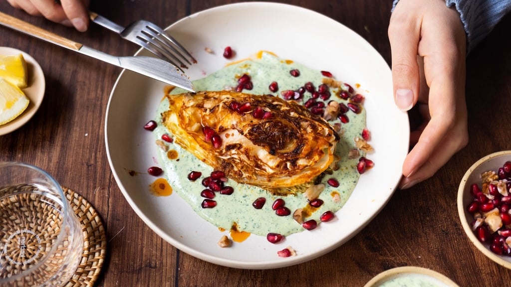 Die Spitzkohl-Viertel werden vor dem Backen kurz in der Pfanne angebraten. Nach 40 Minuten im Ofen werden sie auf Kräuterjoghurt gebettet und mit Granatapfelkernen und Walnüssen getoppt.