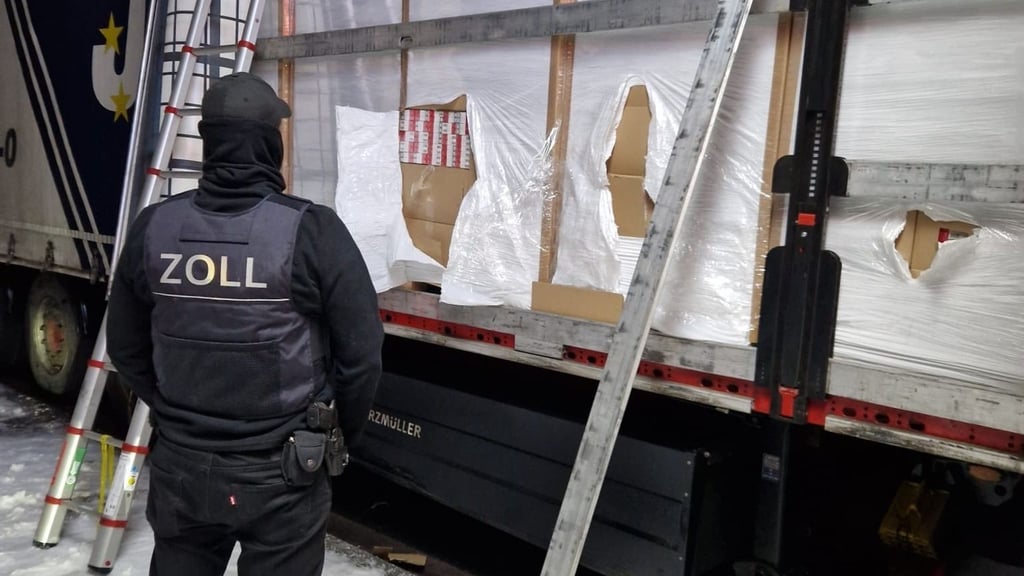 Ein Zöllner steht vor einem mit Zigaretten beladenem Lkw.