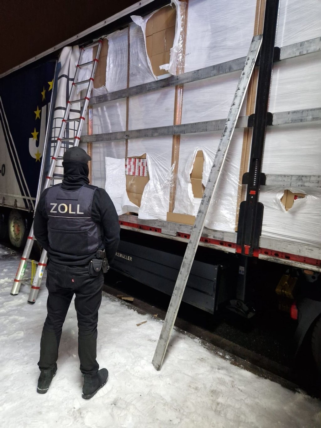Ein Zöllner steht vor einem mit Zigaretten beladenem Lkw.