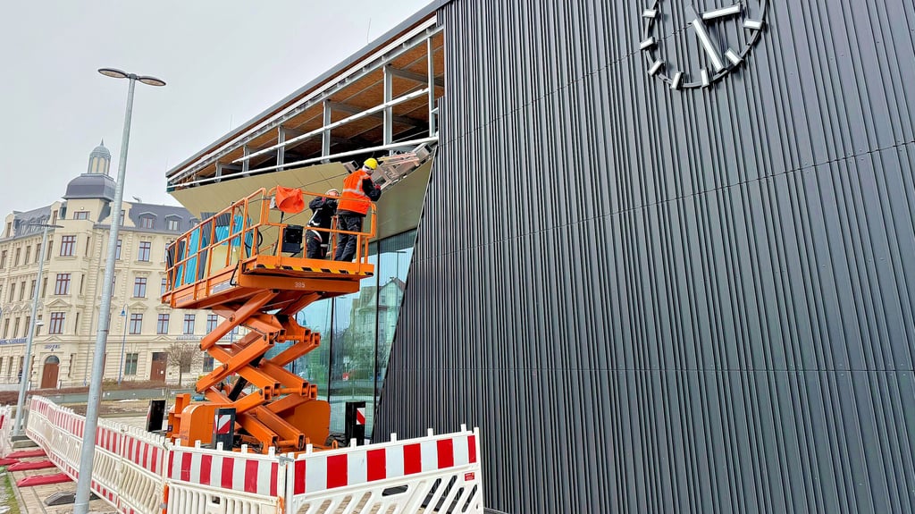 Jörg Fross und Ricky Schirmer bauen von der Hubbühne aus die Fassade des neuen Bitterfelder Bahnhofs vorerst wieder ab. 