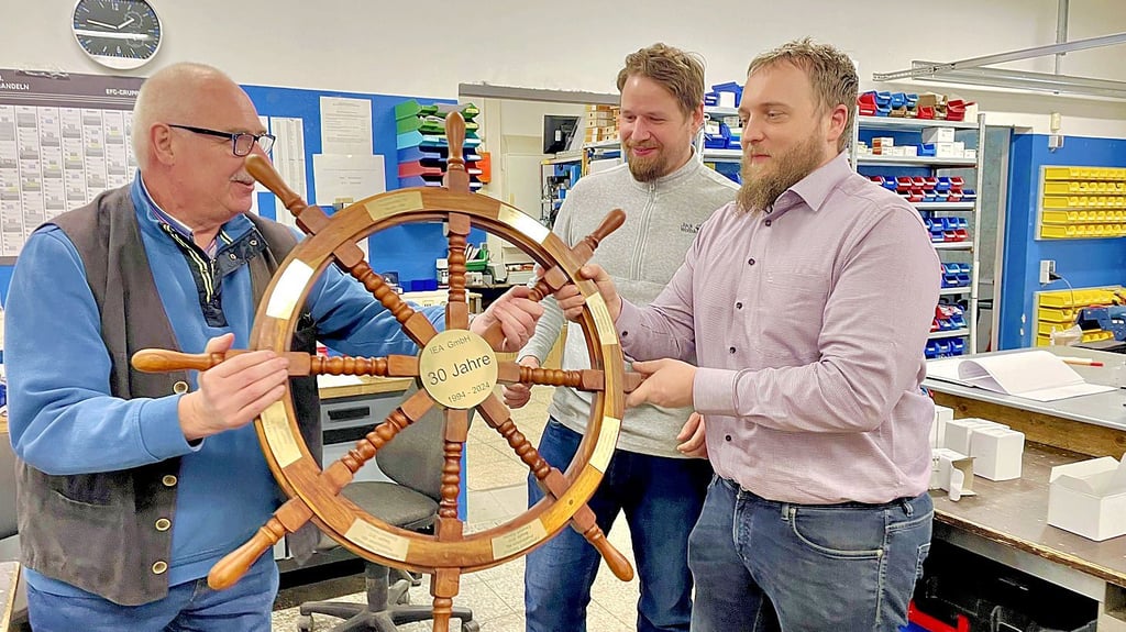 Andreas Planke (l.) übergibt symbolisch mit dem Steuerrad die Geschicke der Firma in die Hände von Thomas Prause (M.) und Thomas Schmechtig