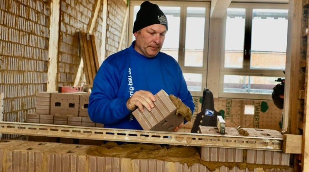 Stein auf Stein: Maurer Thomas Gelhardt baut an einer Lehmsteinwand, mit der die vorgefertigte Holzkonstruktion ausgefacht wird.