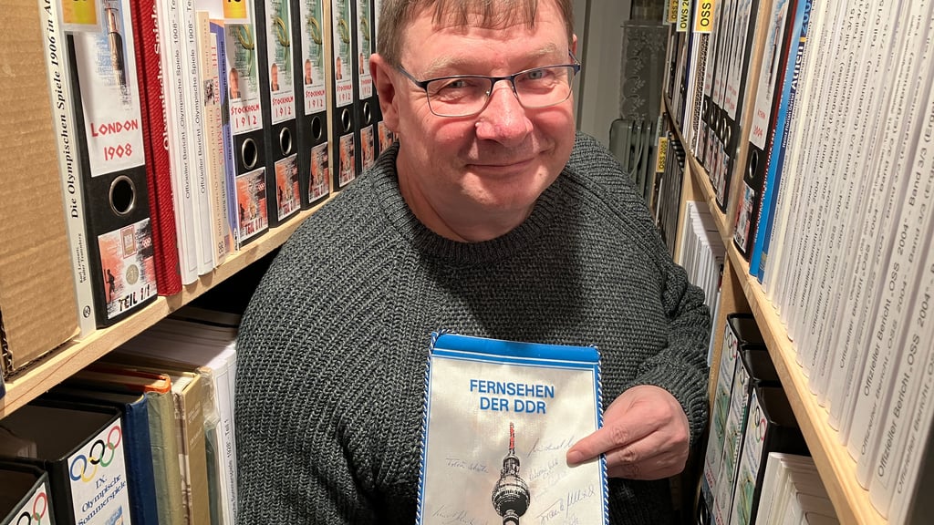 Lutz Seeber in seinem Sportarchiv. Den Wimpel mit Unterschriften von Olympioniken, wie der Eiskunstläuferin Katarina Witt, hatte er bei einem Preisrätsel des Fernsehens der DDR gewonnen. 