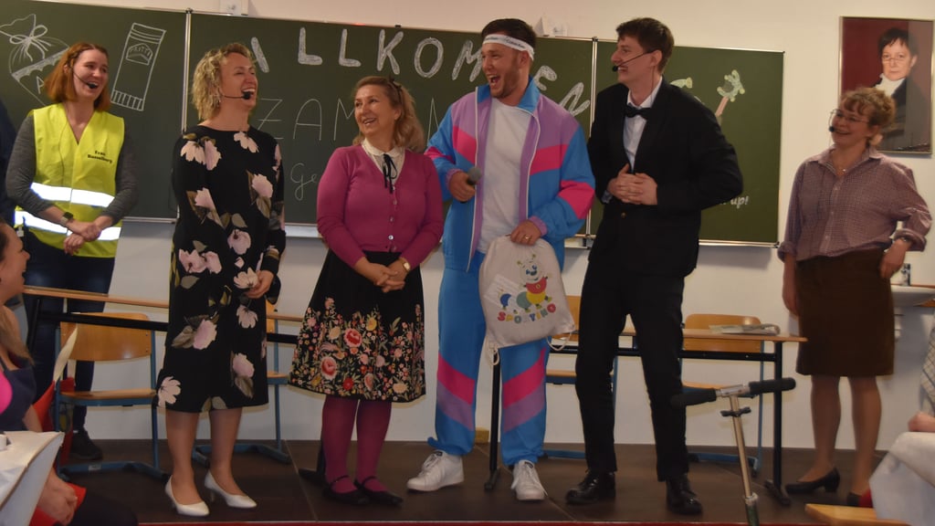 Auch der echte Bürgermeister Marc Blanck (3.v.r.) und Ortsbürgermeisterin Bogumila Jacksch (3.vl.) werden auf die Bühne gebeten. Blanck erscheint im Trainingsanzug – mit Sportbefreiung, versteht sich. Die Ortschefin zeigt sich begeistert vom „Schulprogramm“. Beide Stadtoberhäupter überreichen jeweils Knisterumschläge mit Geldscheinen für den Verein.