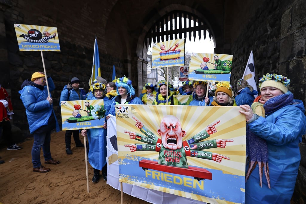 Der ukrainische Hilfsverein Blau-Gelbes-Kreuz hält Plakate mit Putin-Motiven hoch. Das ist als Zeichen der Solidarität mit Wagenbauer Jacques Tilly gemeint. Dieser wird in Russland strafrechtlich verfolgt.