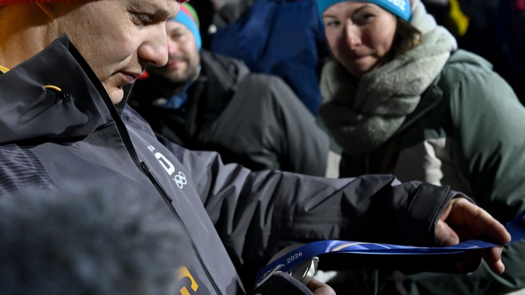 Francesco Friedrich betrachtet nach der Siegerehrung seine Silbermedaille neben seiner Frau Magdalena.