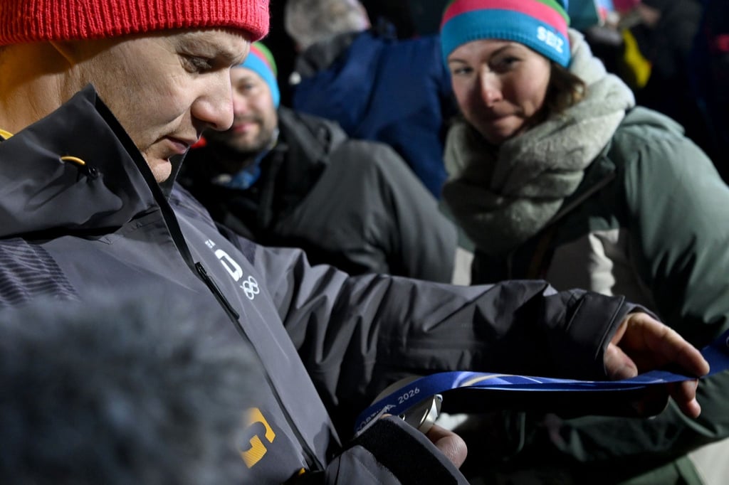 Francesco Friedrich betrachtet nach der Siegerehrung seine Silbermedaille neben seiner Frau Magdalena.