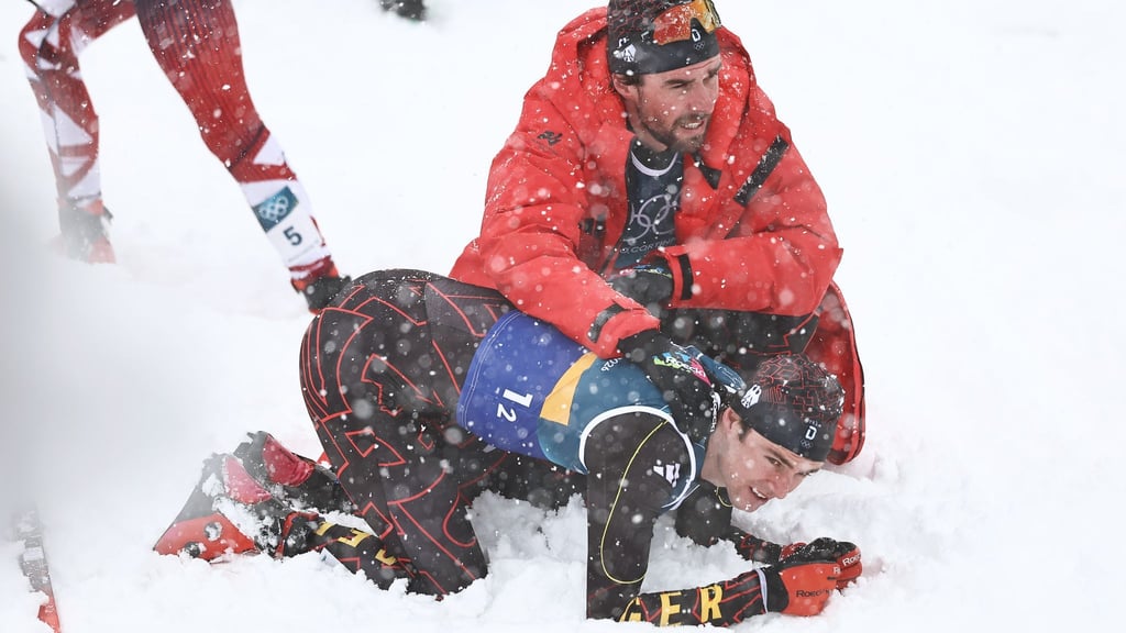 Vinzenz Geiger liegt im Schnee und wird von Teamkollege Johannes Rydzek getröstet.