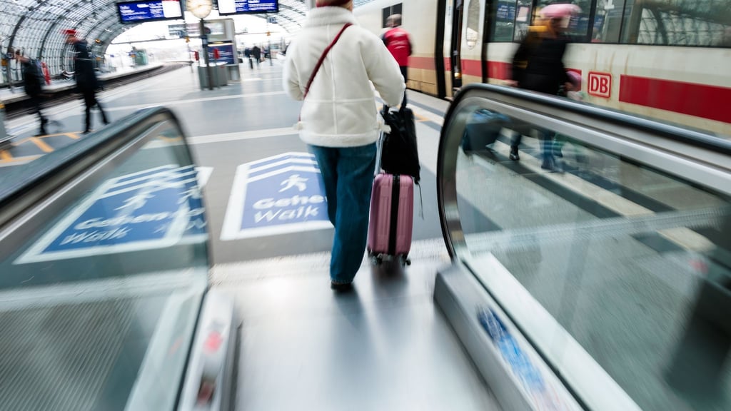 Eine Reisende fährt am Berliner Hauptbahnhof mit ihrem Koffer eine Rolltreppe zum Bahnsteig hinauf.