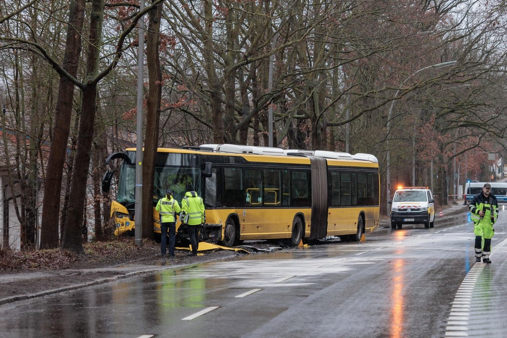 Polizisten stehen an einer Unfallstelle vor einem beschädigten Bus.