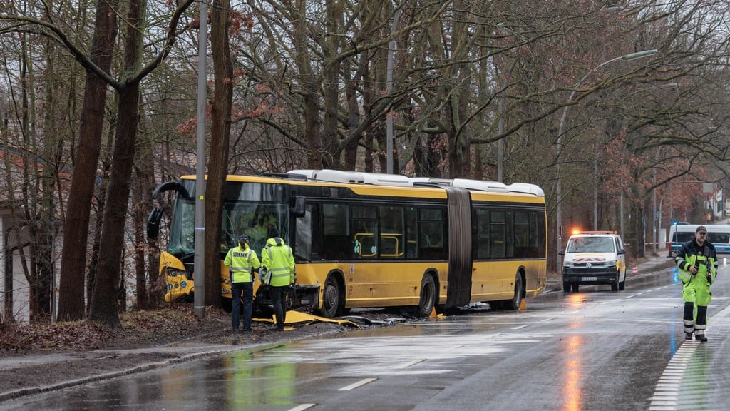 Polizisten stehen an einer Unfallstelle vor einem beschädigten Bus.