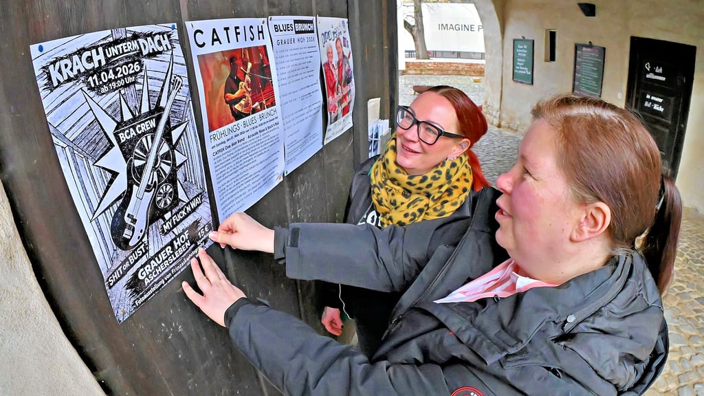 Corina Friebel (vorn) und Katja Ciesilski hängen die Plakate für „Krach unterm Dach“ auf – wie hier am Tor des Grauen Hofs.