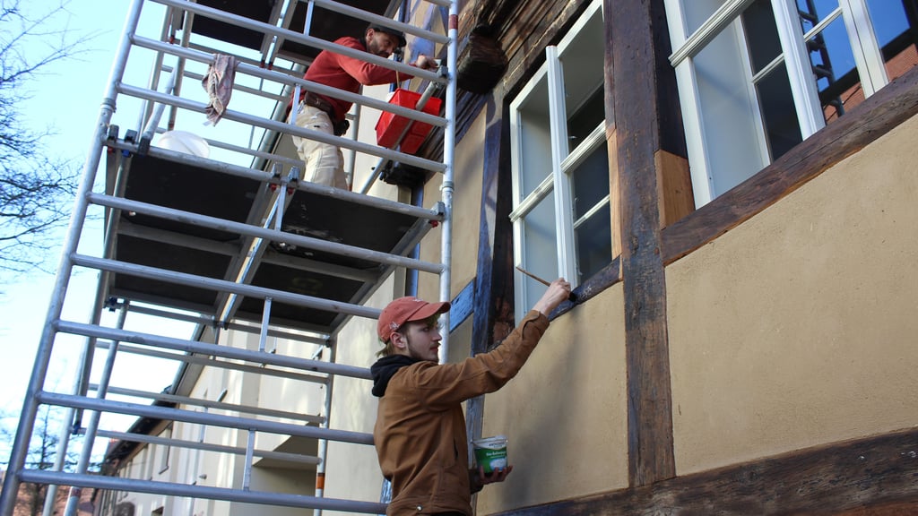 Dirk Knüpfer (oben) und Linus Moske aus Halle streichen mit Leinöl das Gebälk des Ratsfischerhauses in der Stendaler Straße.