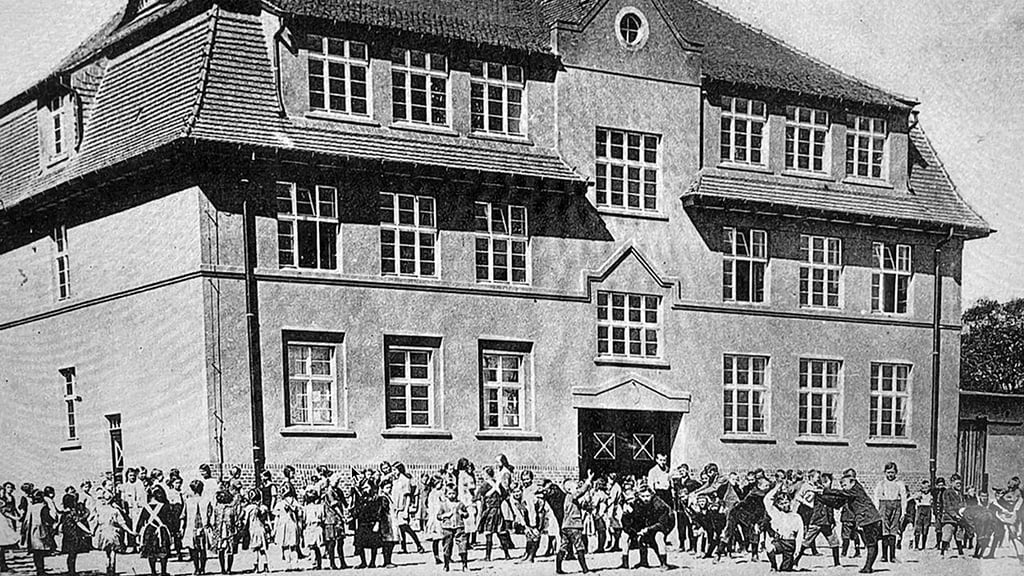 Diese alte Ansicht der Schule zeigt noch ein Fenster anstelle der Uhr im Giebel. Die Schule wurde 1926 eingeweiht, erst 1928 kam die Uhr dazu. 