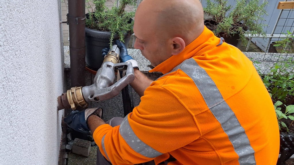 Ein Mitarbeiter eines Brennstoffhändlers füllt an einem Haus einen Heizöltank.