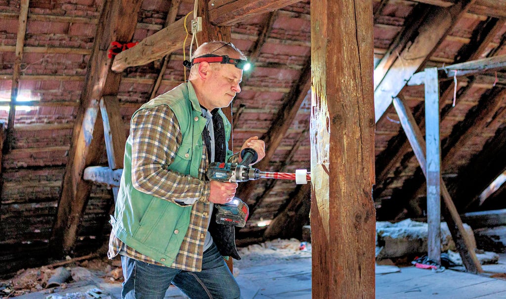 Die Bauhistoriker Torsten Lieberenz bohrt aus einem Balken im Dachstuhl des Hauses ein sogenanntes Dendro (rundes Bild) heraus.  