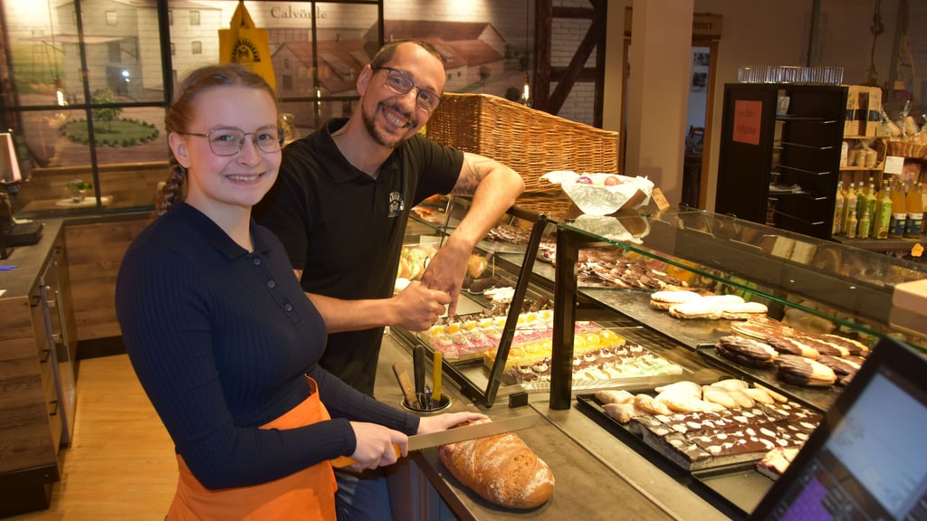 Calvördes Bäckermeister Denni Nitzschke schaut der Auszubildenden Kyra Lübke über die Schulter, während sie geschickt in der Schaubäckerei Brot frisch für die Kundschaft schneidet.